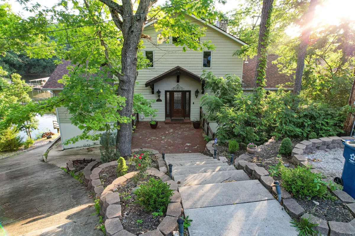 A welcoming front entrance set along a stone pathway and landscaped garden, framed by lush greenery. The scene feels inviting, blending the comfort of home with the seclusion of nature.