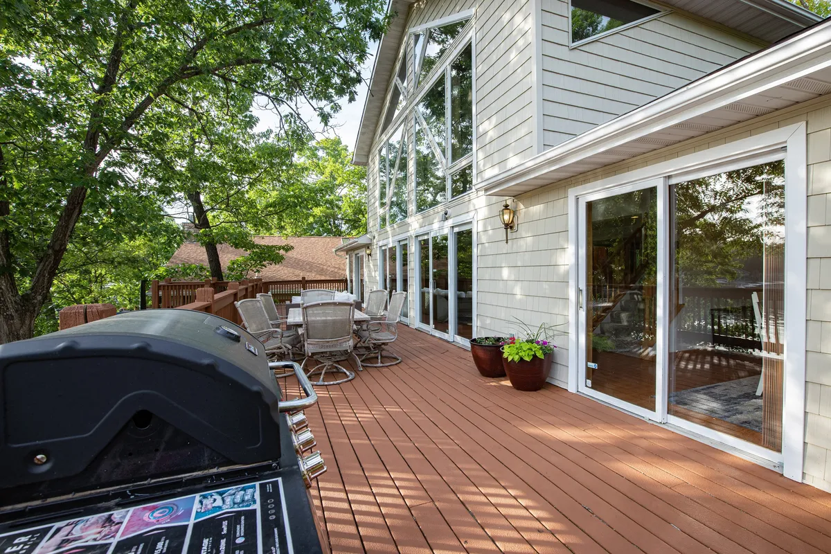 Looking from the deck, this exterior image features large glass windows, an outdoor dining area, and a grill, all set for barbecues and gatherings. The direct connection from the interior to the deck is visible, inviting guests to flow easily between inside and outside social spaces.