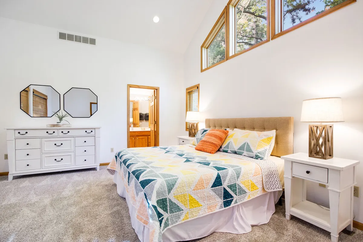 A tranquil bedroom scene featuring a bed with a colorful quilt, two bedside tables with lamps, and decorative mirrors on the wall. The room is softly lit by natural light, inviting relaxation and restful sleep.