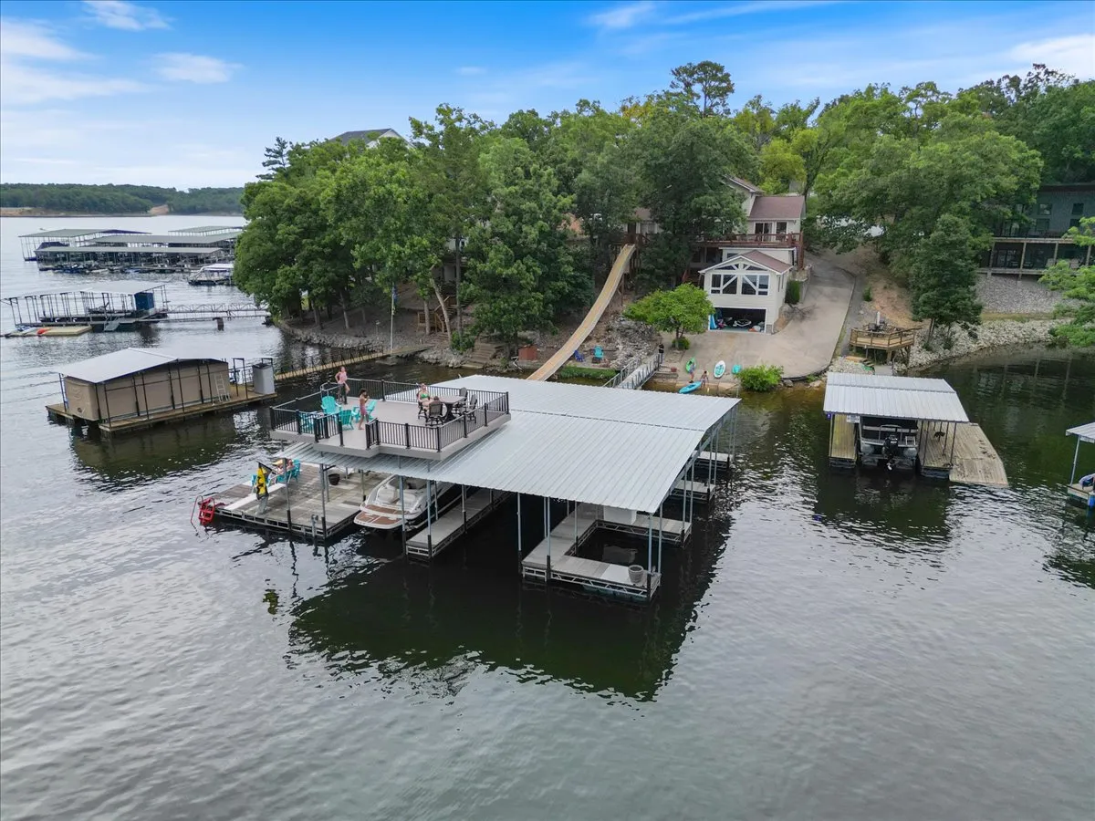 A spacious private dock with a boathouse, surrounded by water, trees, and a patio area. The dock includes a seating area perfect for relaxing or enjoying snacks and drinks by the lake.
