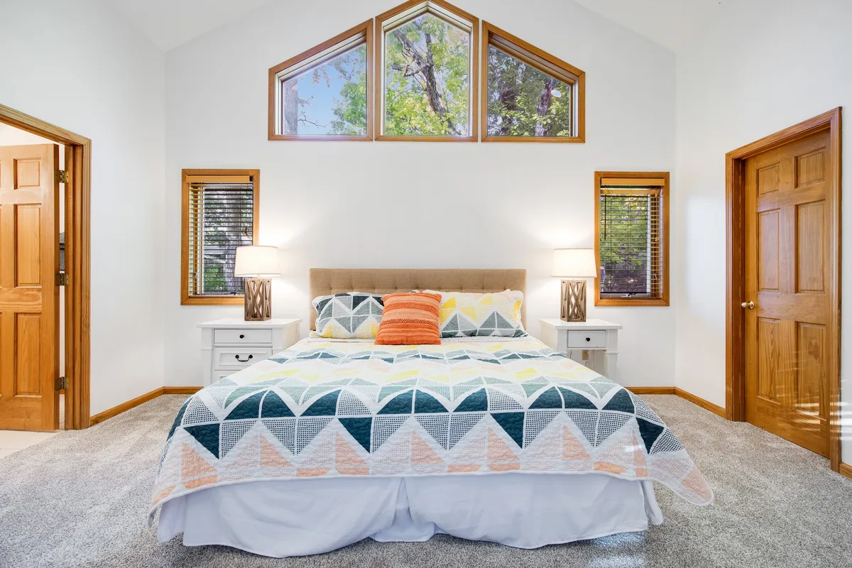 A cozy king suite featuring a comfortable bed adorned with decorative pillows, flanked by nightstands and lamps, with soft natural light filtering through large windows, creating a tranquil and inviting atmosphere ideal for relaxation and privacy.