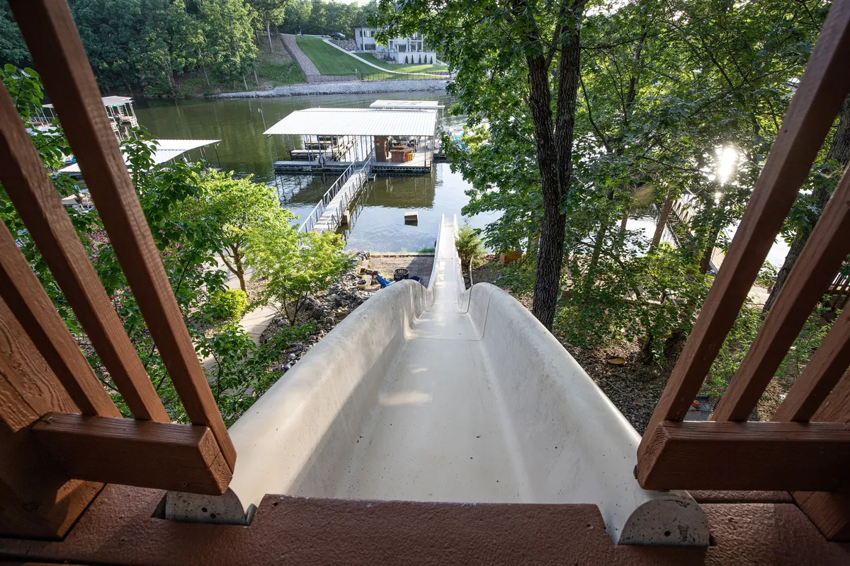 This exterior image captures the engineered water slide descending from the dock into the lake, with the waterfront, dock, and surrounding trees all in view. The playful scene suggests opportunities for swimming, boating, and family fun, all under a bright summer sky.