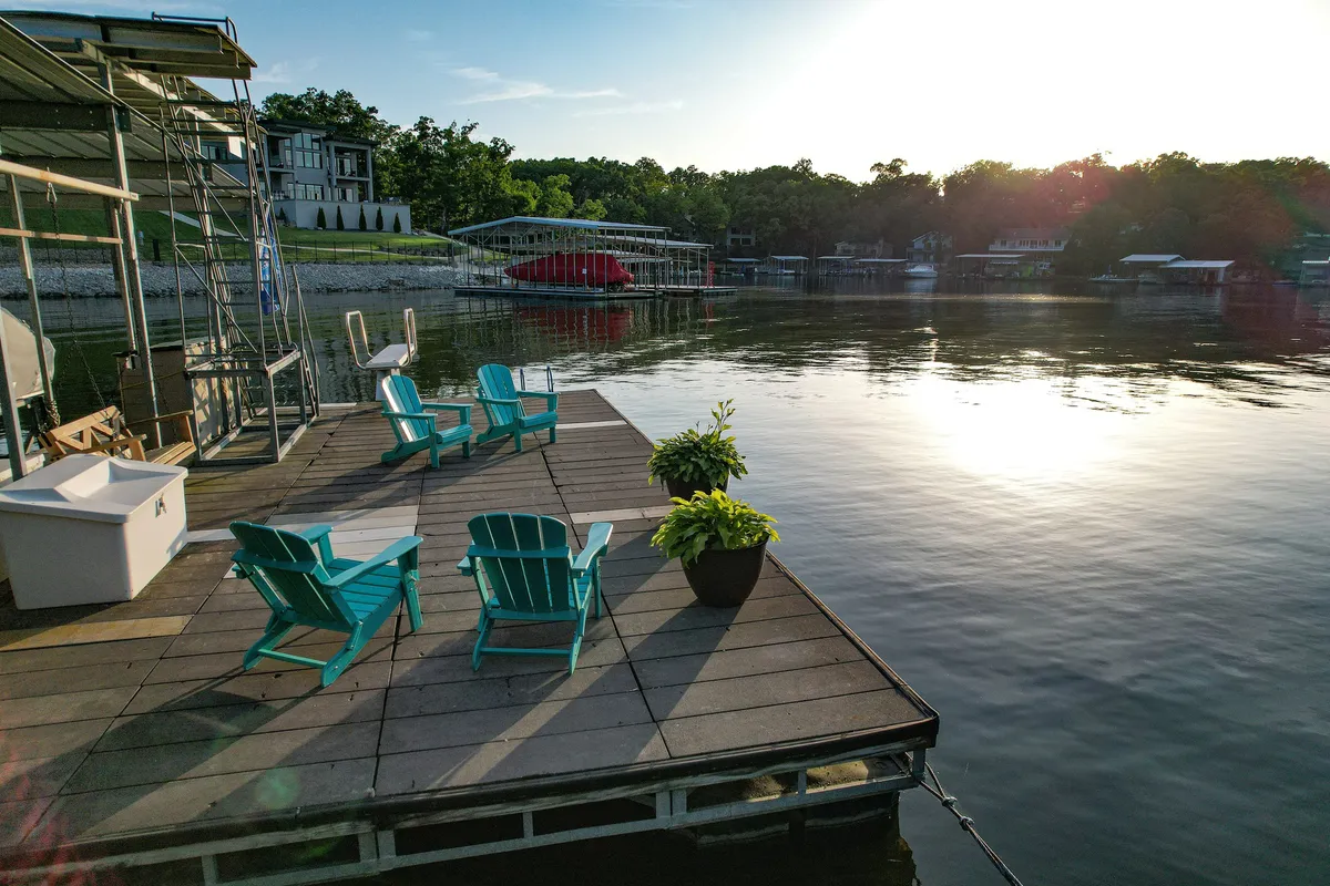 A cozy dock scene with Adirondack chairs, a potted plant, and a tranquil view of the water at sunset. The warm light and calm setting evoke relaxation and shared moments by the lake.