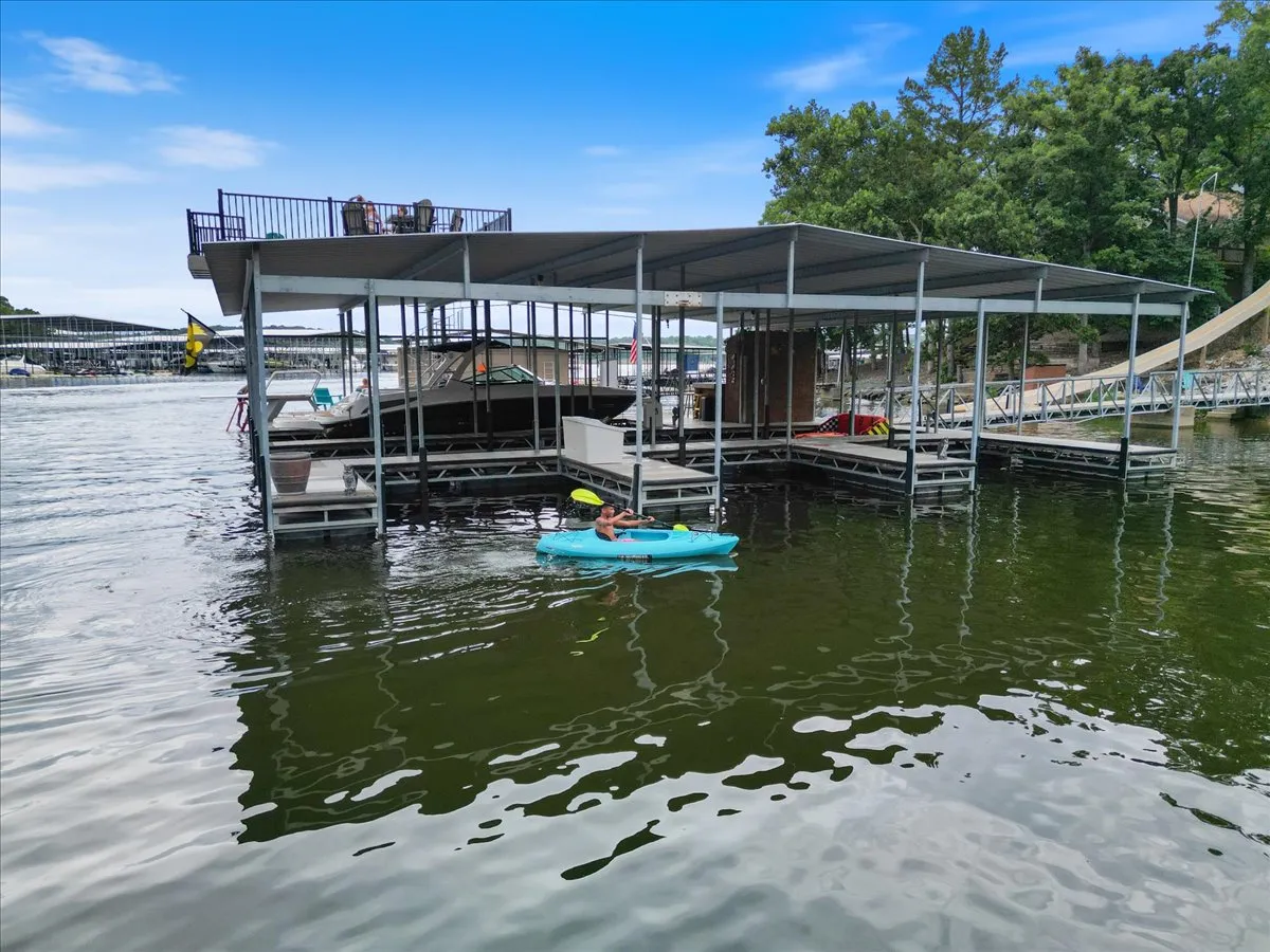 A dock extending over the water with a kayak and boats nearby. Lush trees surround the area, creating a tranquil lakeside atmosphere ideal for water sports and relaxation.